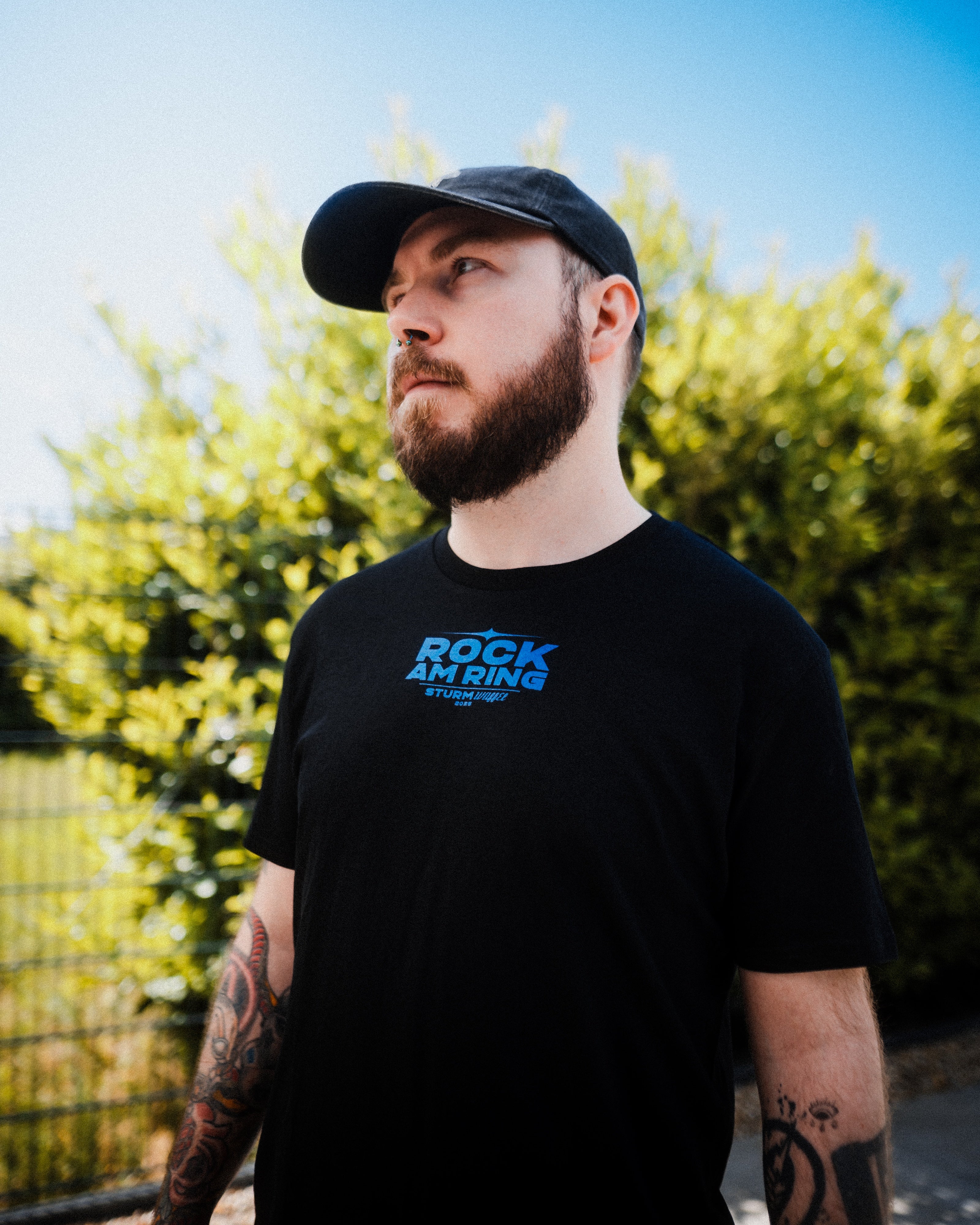 Mann mit Cap und Tattoos modelt das Sturmwaffel x Rock am Ring - Unisex T-Shirt - Schwarz